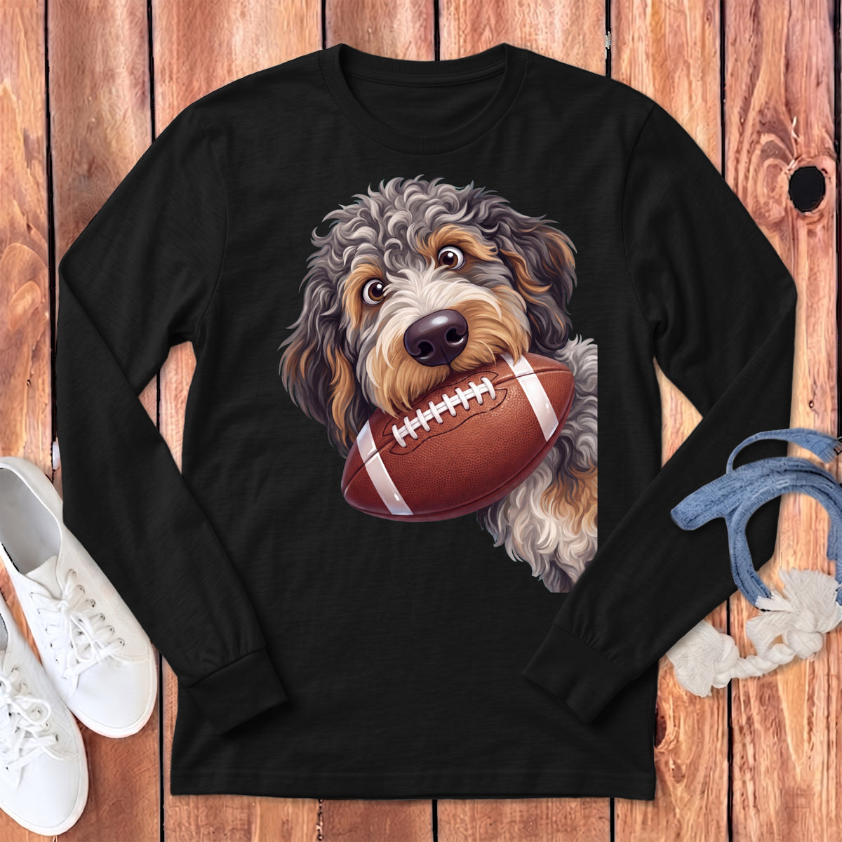 Black long-sleeve t-shirt featuring a doodle dog holding a football in its mouth, displayed on wood.