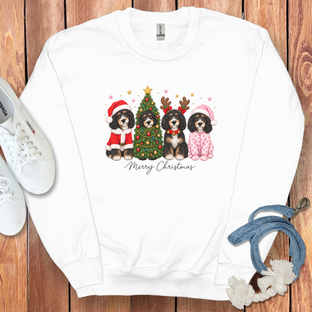 A white crewneck sweatshirt features a graphic of four doodle dogs celebrating Christmas with a tree and the text Merry Christmas.