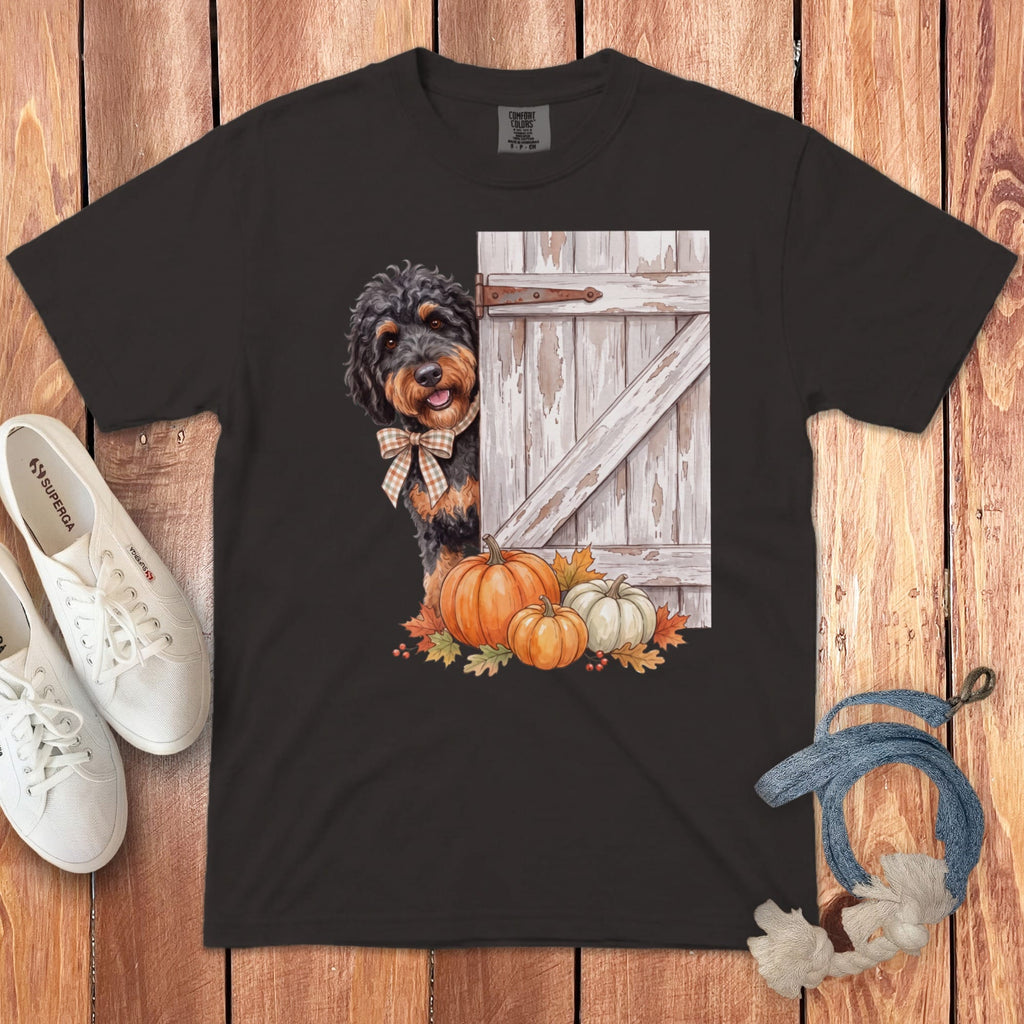 Dark t-shirt with watercolor print of a dog peeking around a barn door with pumpkins.
