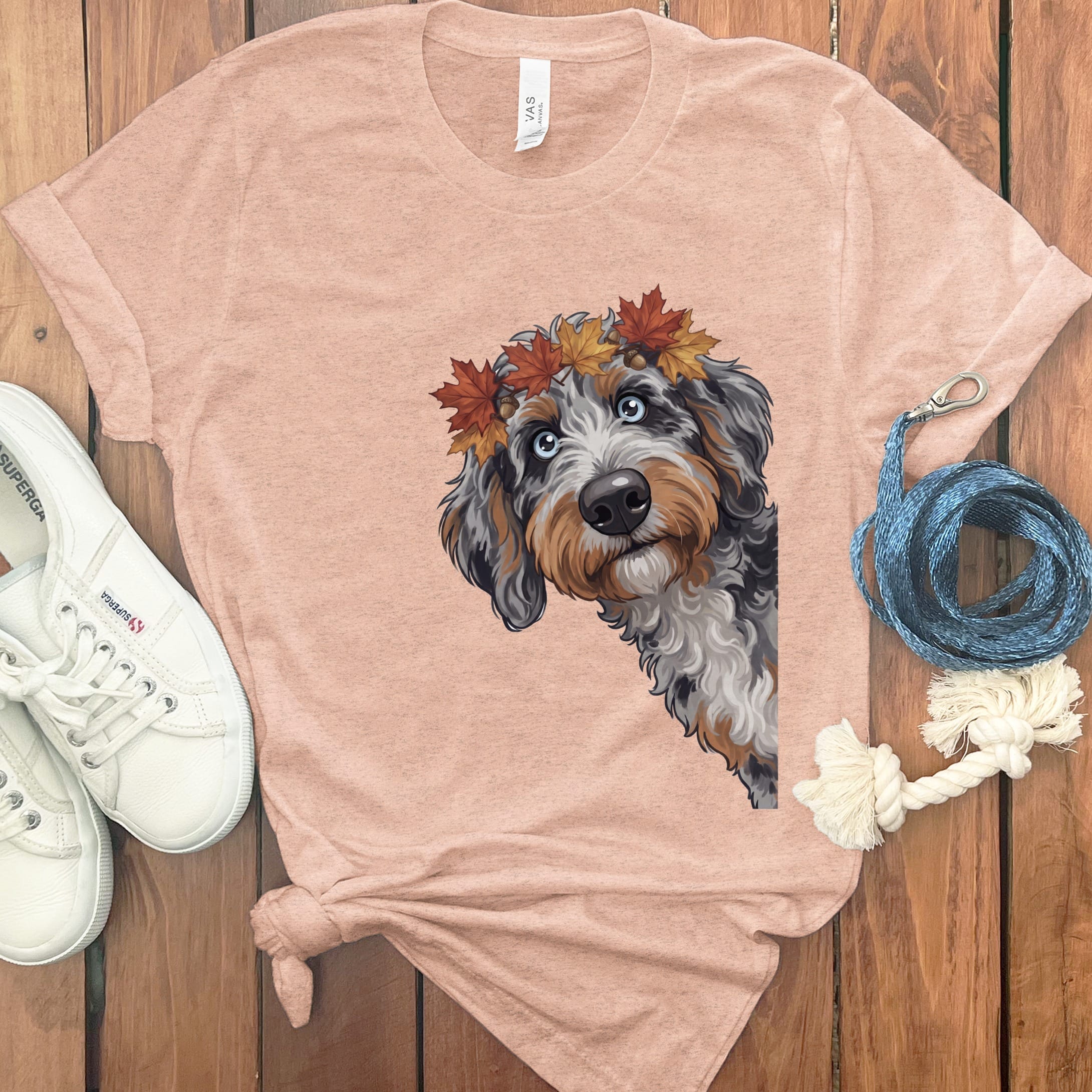 Sheepadoodle dog wearing a fall leaf crown on a peach t-shirt.