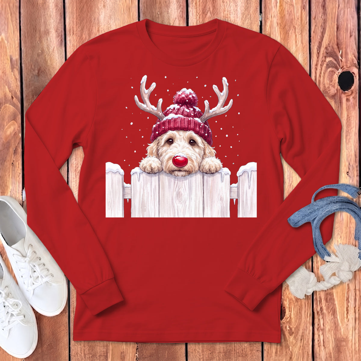 A doodle dog wearing a Santa hat and antlers peeks over a snowy fence.