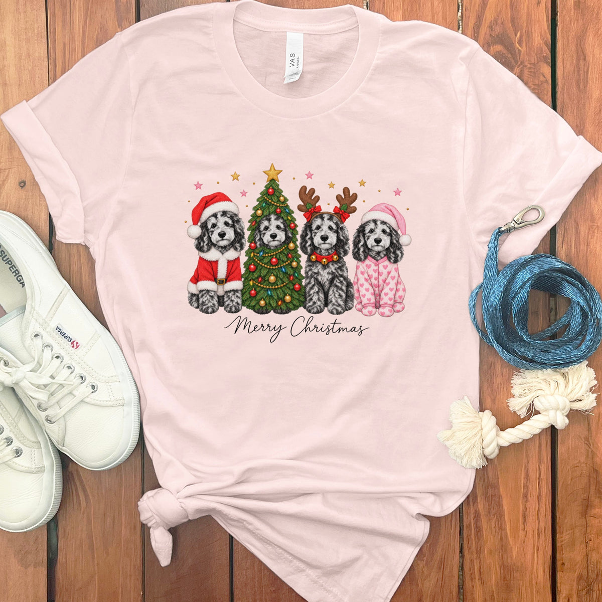 A light pink t-shirt with a graphic of four festive dogs and the text Merry Christmas.