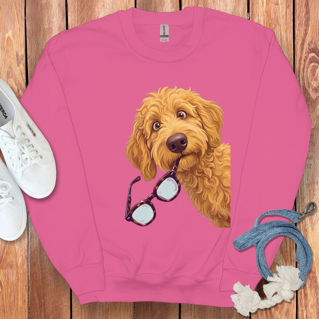 Pink crewneck sweatshirt featuring a graphic of a golden doodle dog holding tortoiseshell glasses in its mouth.