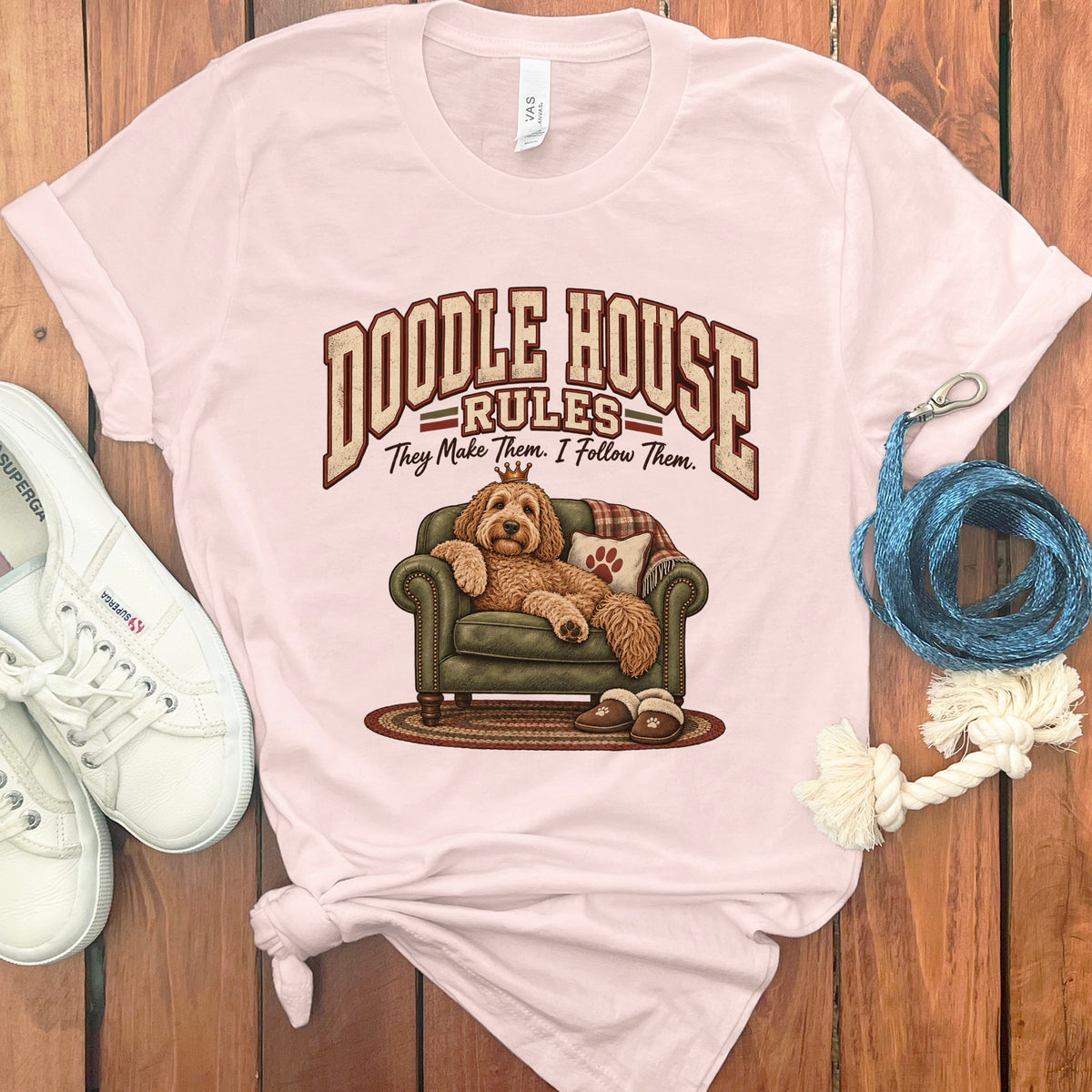 Pink t-shirt with a doodle dog wearing a crown sitting on a couch.