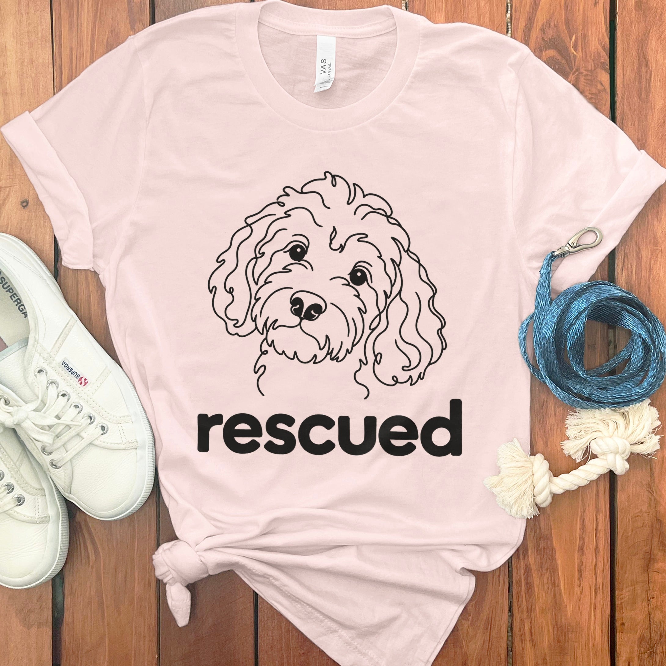 Light pink t-shirt with line drawing of dog face and text "rescued".