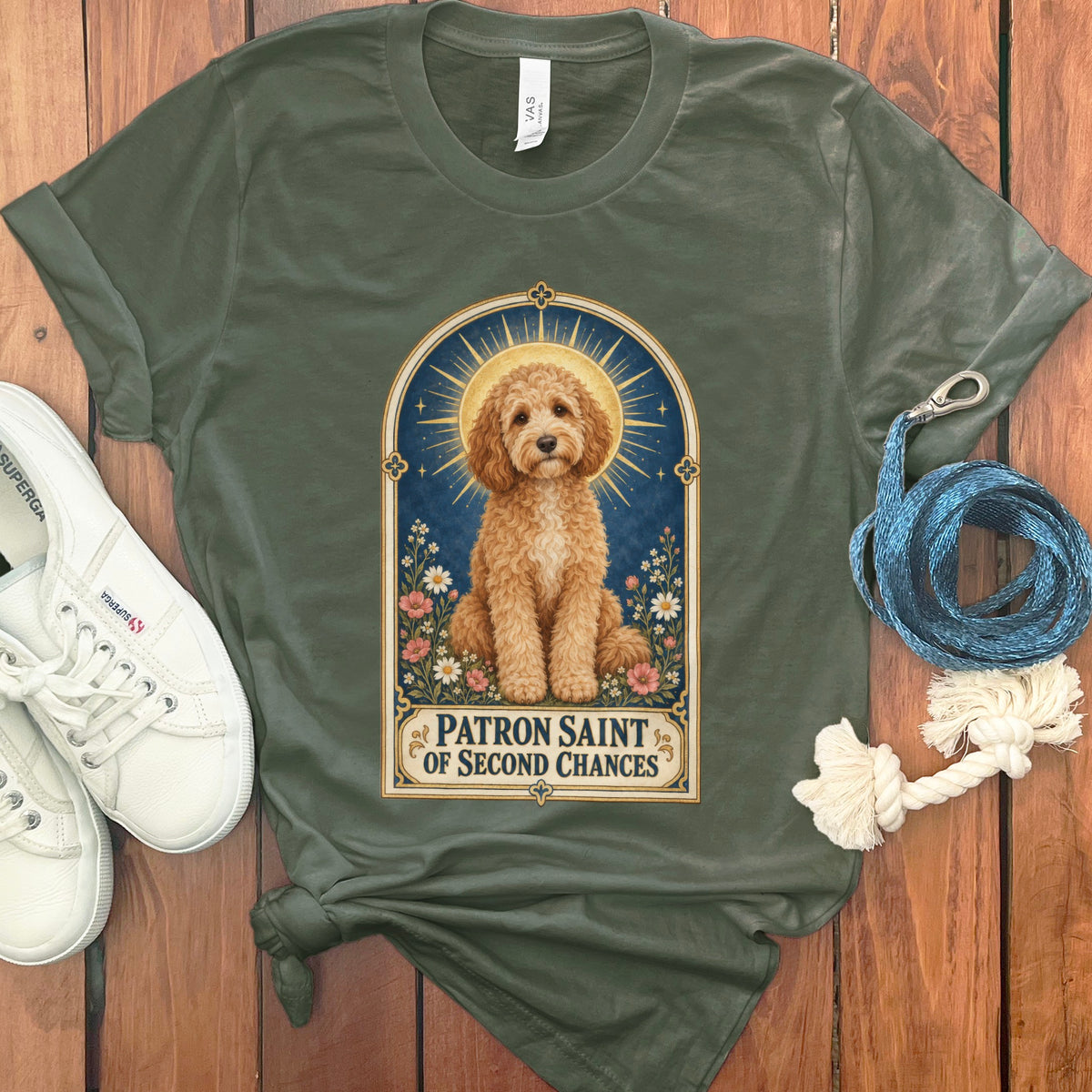 Olive green t-shirt with a gold-haloed dog and text "PATRON SAINT OF SECOND CHANCES."