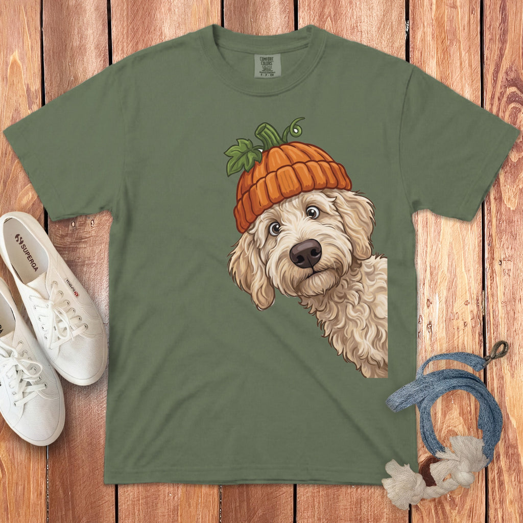 Labradoodle wearing an orange pumpkin hat peeks from the right on a green t-shirt.