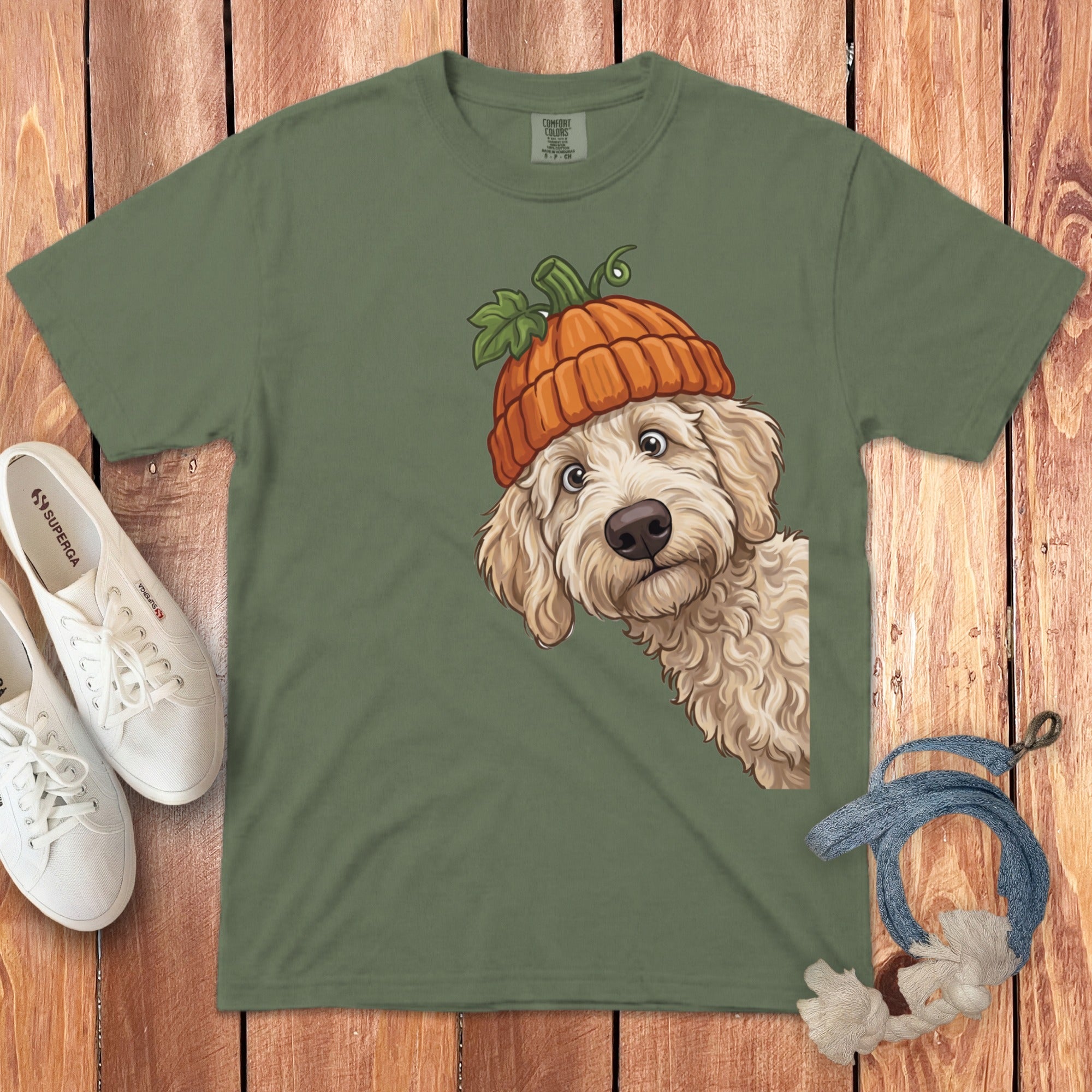 Labradoodle wearing an orange pumpkin hat peeks from the right on a green t-shirt.