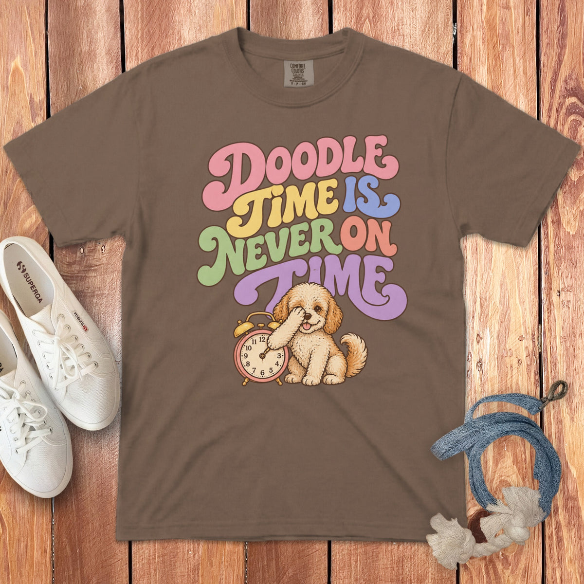 Brown t-shirt featuring a cartoon doodle puppy covering its face next to a clock and retro text reading Doodle Time is Never on Time.