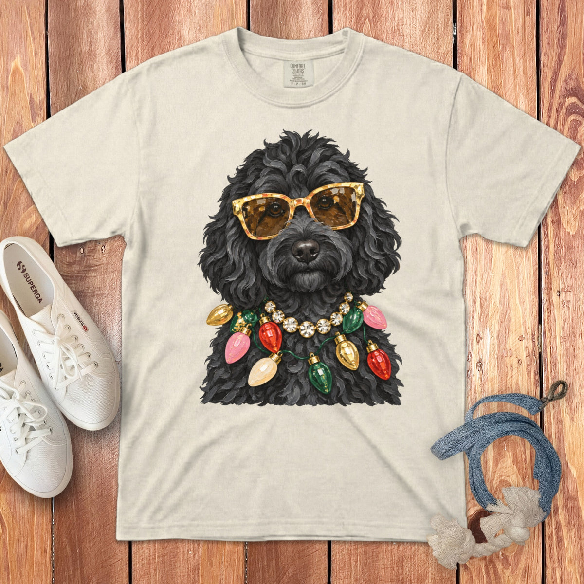 Black dog wearing sunglasses and a colorful Christmas light necklace on a cream t-shirt.
