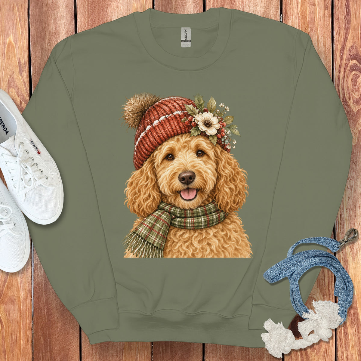 Goldendoodle wearing a knitted hat and plaid scarf with floral accents on olive sweatshirt.
