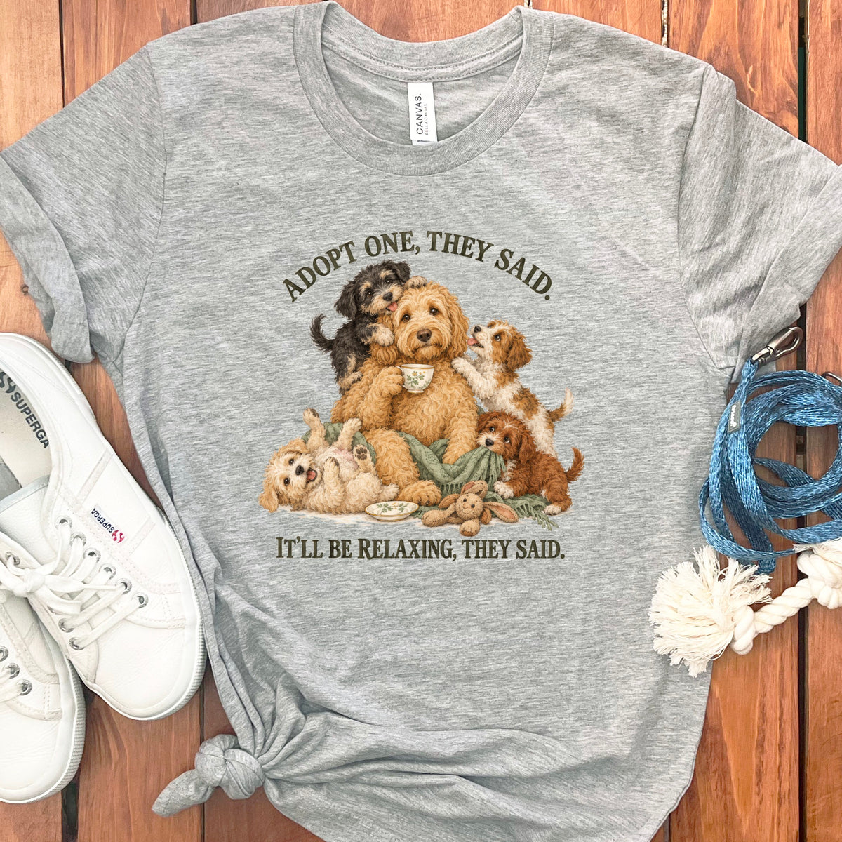 Grey t-shirt with illustration of fluffy dogs and text: "ADOPT ONE, THEY SAID. IT'LL BE RELAXING, THEY SAID."