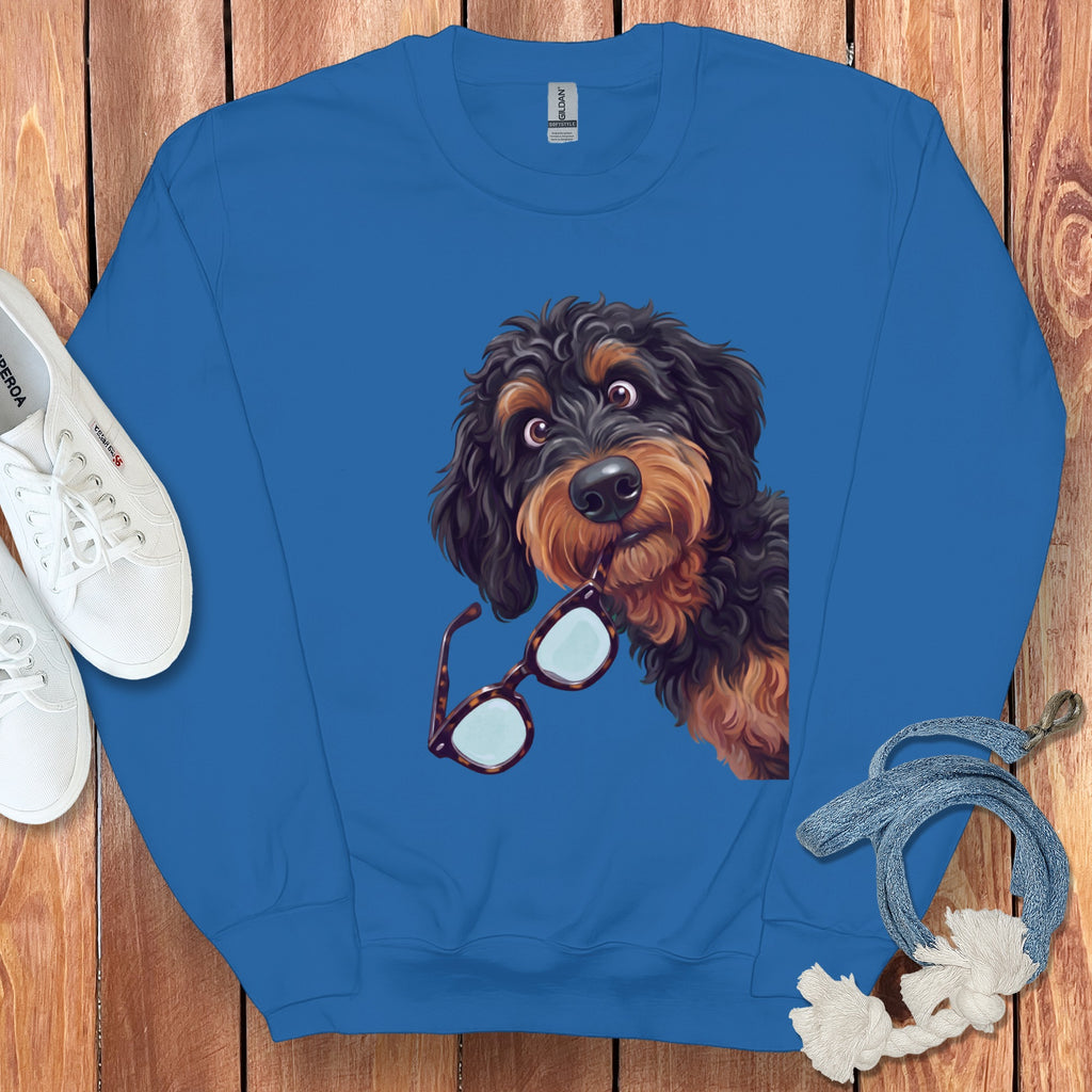Blue crewneck sweatshirt featuring a graphic of a black and brown fluffy dog holding glasses in its mouth.