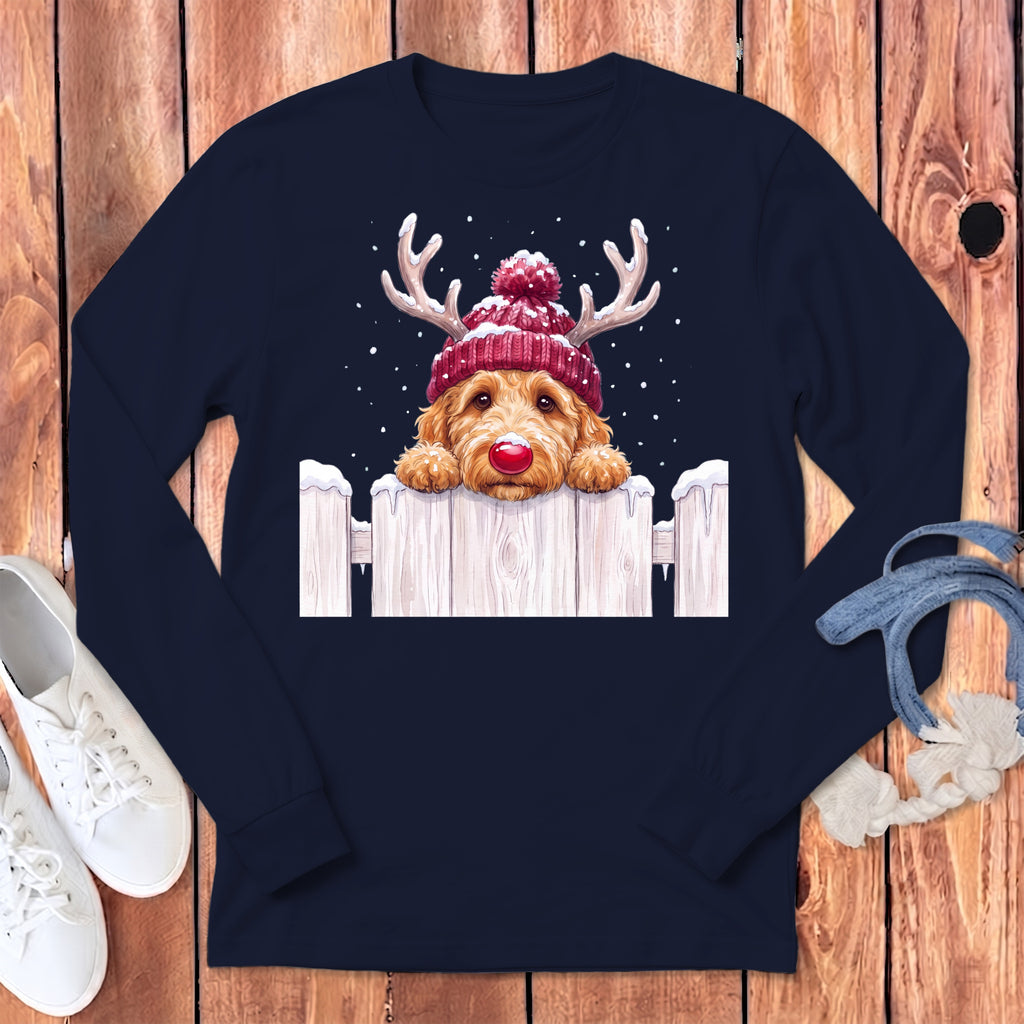Golden doodle dog with reindeer antlers and red nose peeking over a snowy fence.