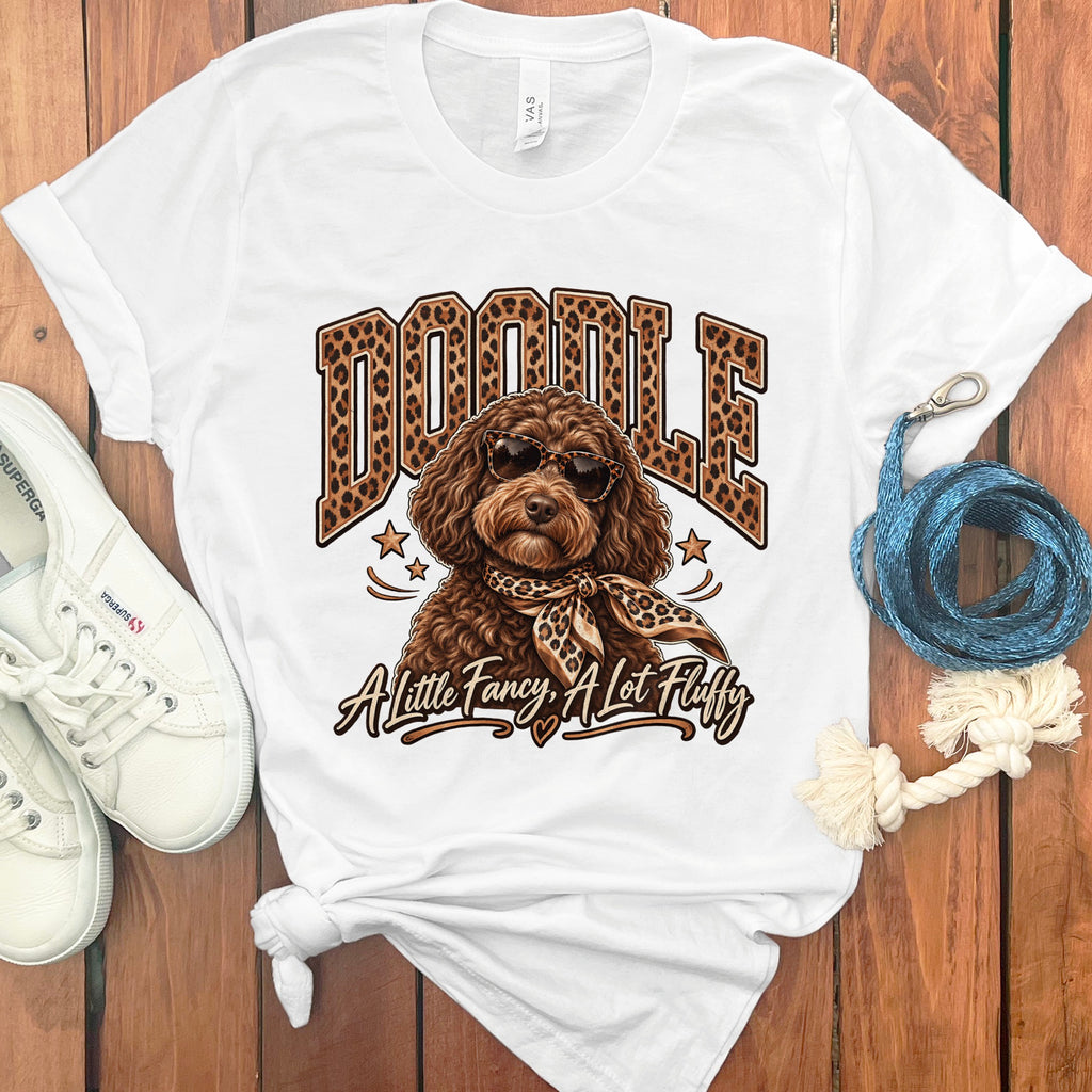 White t-shirt with "DOODLE" text, a dog in sunglasses, and text "A Little Fancy, A Lot Fluffy".