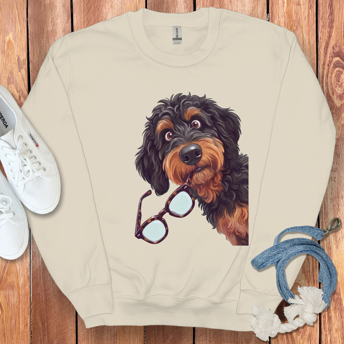 Beige crewneck sweatshirt featuring a graphic of a black and tan doodle dog holding glasses in its mouth.