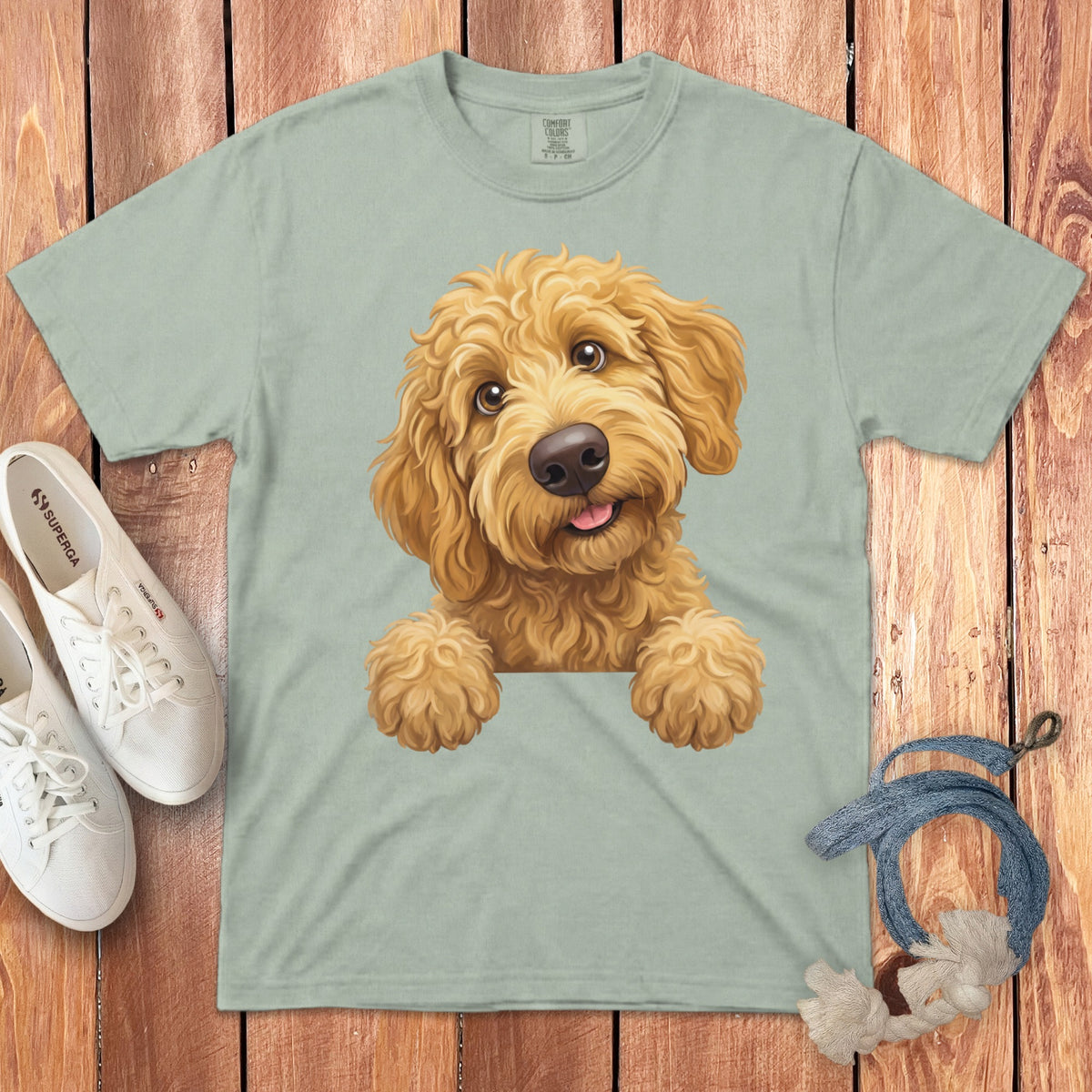 Light green t-shirt with illustration of a happy golden doodle dog peeking over the edge.