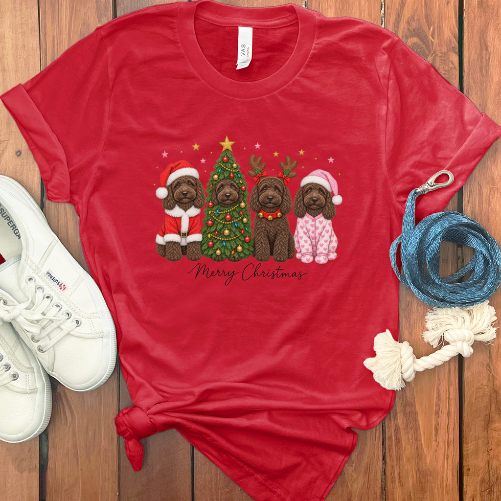 Red t-shirt with a graphic of four doodle dogs celebrating Christmas, surrounded by white sneakers and a blue rope on wood background.