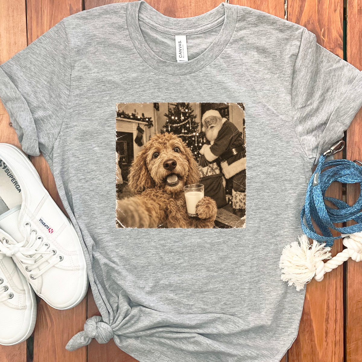 A heather gray crewneck t-shirt featuring a vintage sepia graphic of a golden doodle dog holding a glass of milk with Santa Claus in the background.