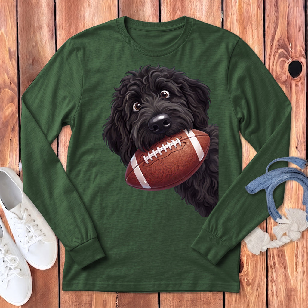 Black doodle dog holding an American football on a green long-sleeve shirt.