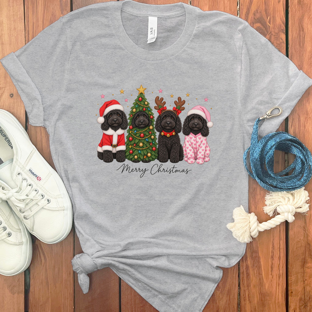 Gray t-shirt featuring four black dogs in holiday costumes and Merry Christmas text, surrounded by white shoes and a blue leash on wood.