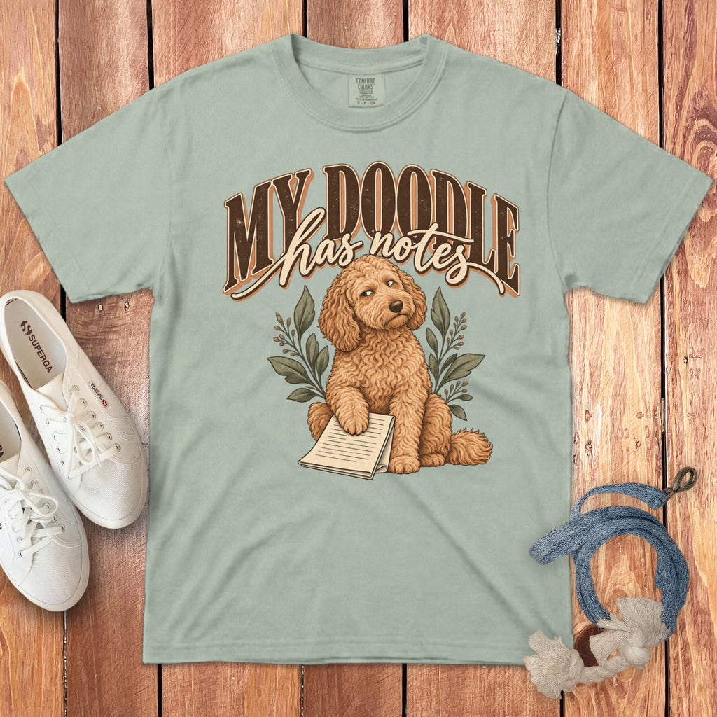 Sage green t-shirt with a graphic of a brown doodle dog, leaf sprigs, and the text My Doodle has notes.