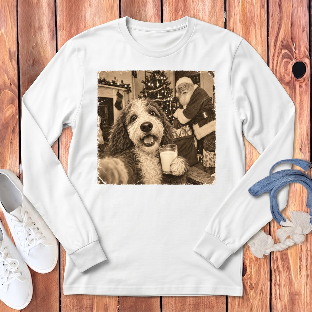 White long-sleeve t-shirt featuring a sepia-toned graphic of a fluffy dog holding a glass of milk while Santa Claus stands in the background.