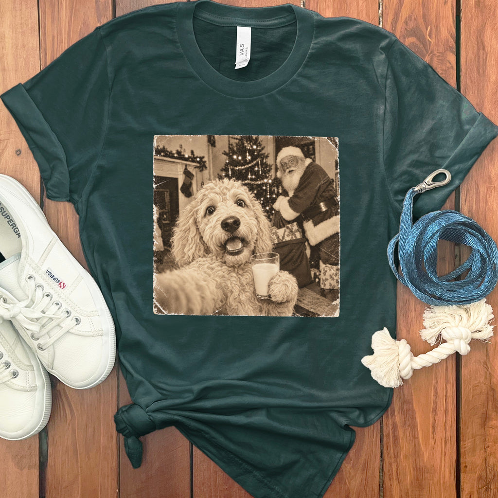 Dark green crewneck t-shirt featuring a retro graphic of a fluffy dog holding a glass of milk with Santa Claus in the background, laid on a wooden surface with white sneakers and a blue leash.