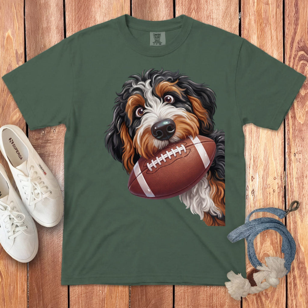 Bernese mountain dog puppy holding a football on a green t-shirt.