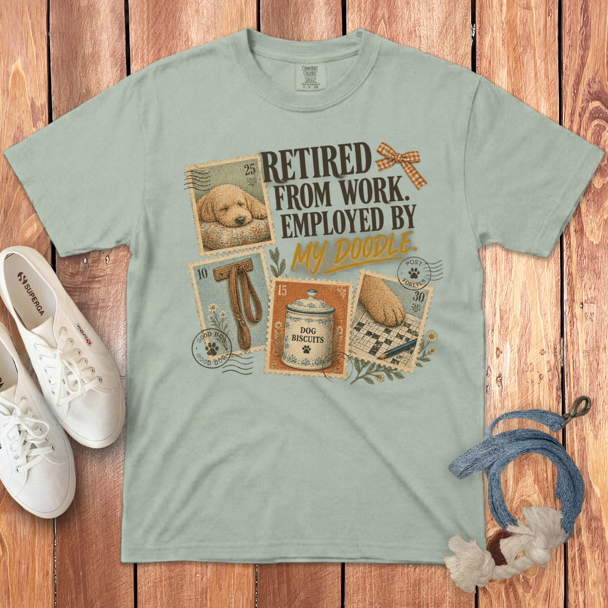 Sage green t-shirt featuring the text RETIRED FROM WORK EMPLOYED BY MY DOODLE alongside dog-themed graphics.