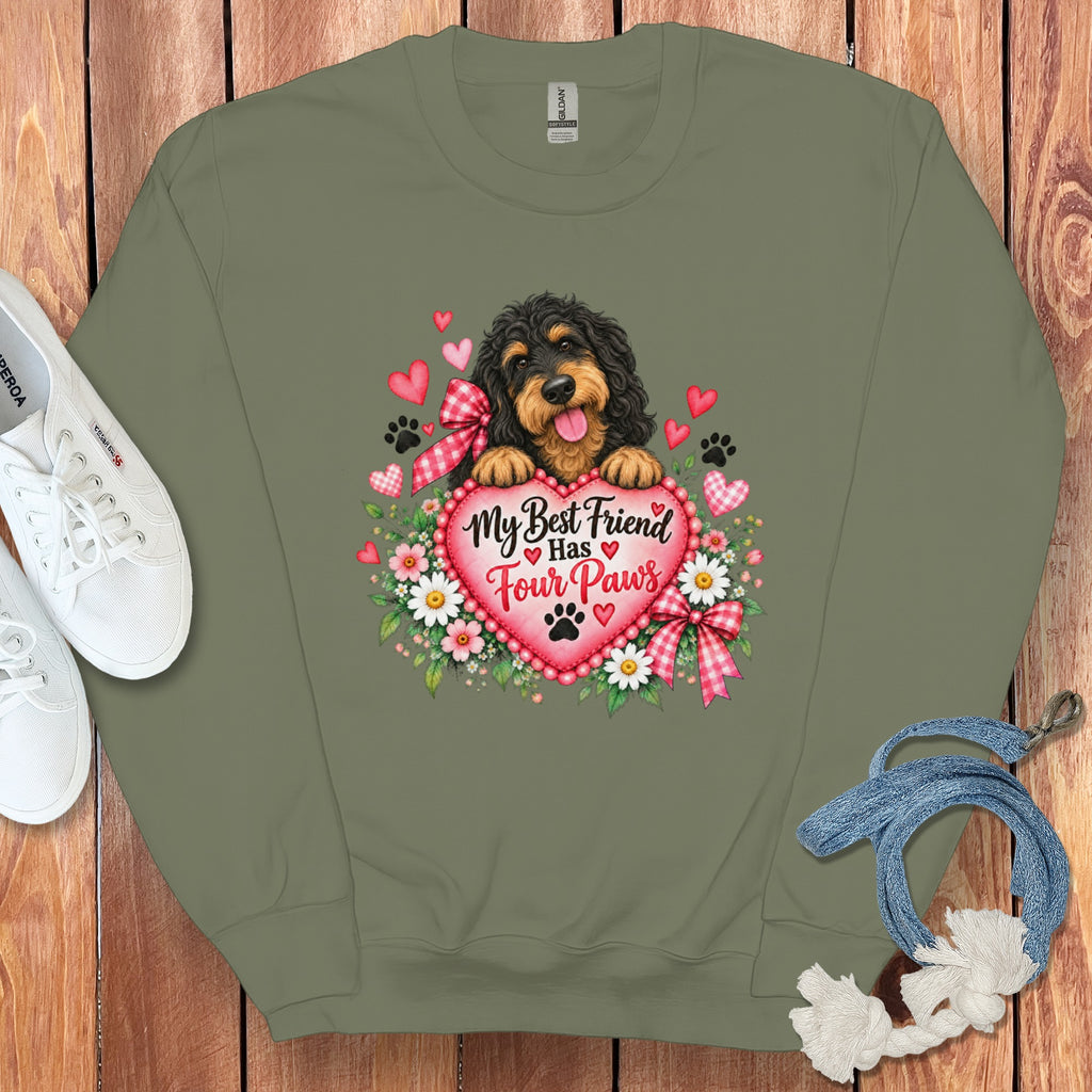 Olive green crewneck sweatshirt featuring a graphic of a Bernedoodle dog holding a heart with text that reads My Best Friend Has Four Paws, surrounded by flowers and paw prints, on a wood background.