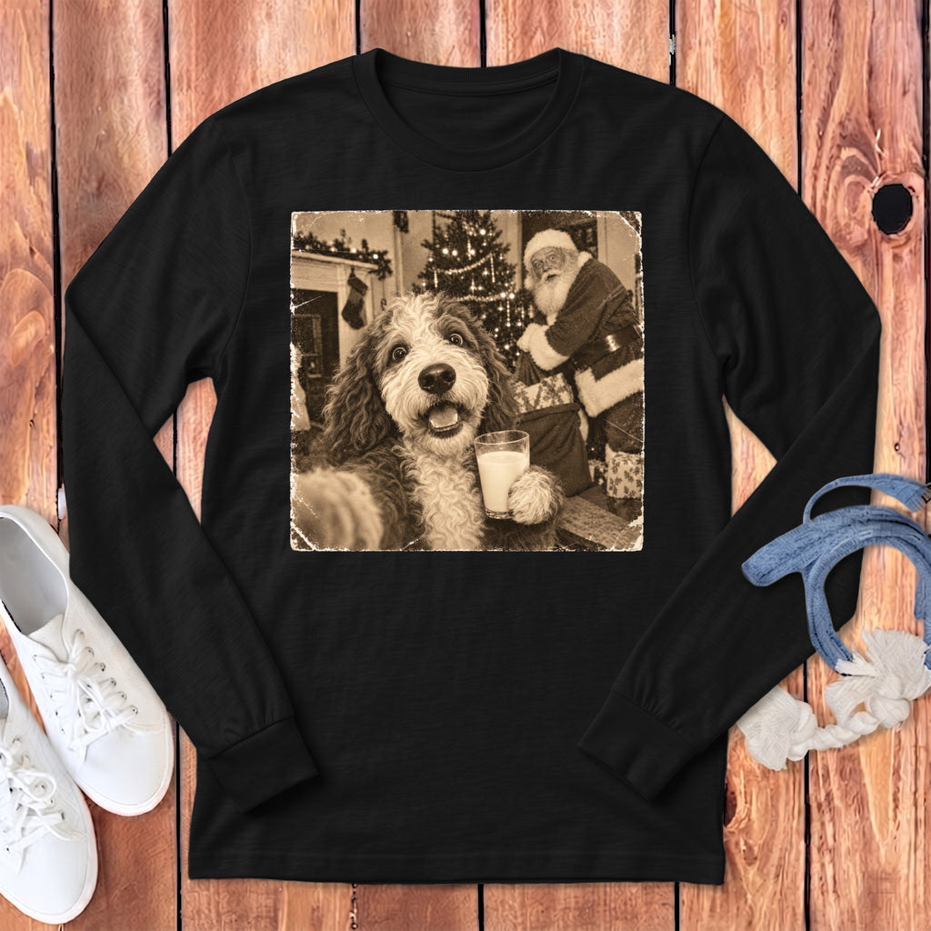 Black long-sleeve t-shirt featuring a sepia-toned graphic of a fluffy dog holding a glass of milk with Santa Claus in the background.