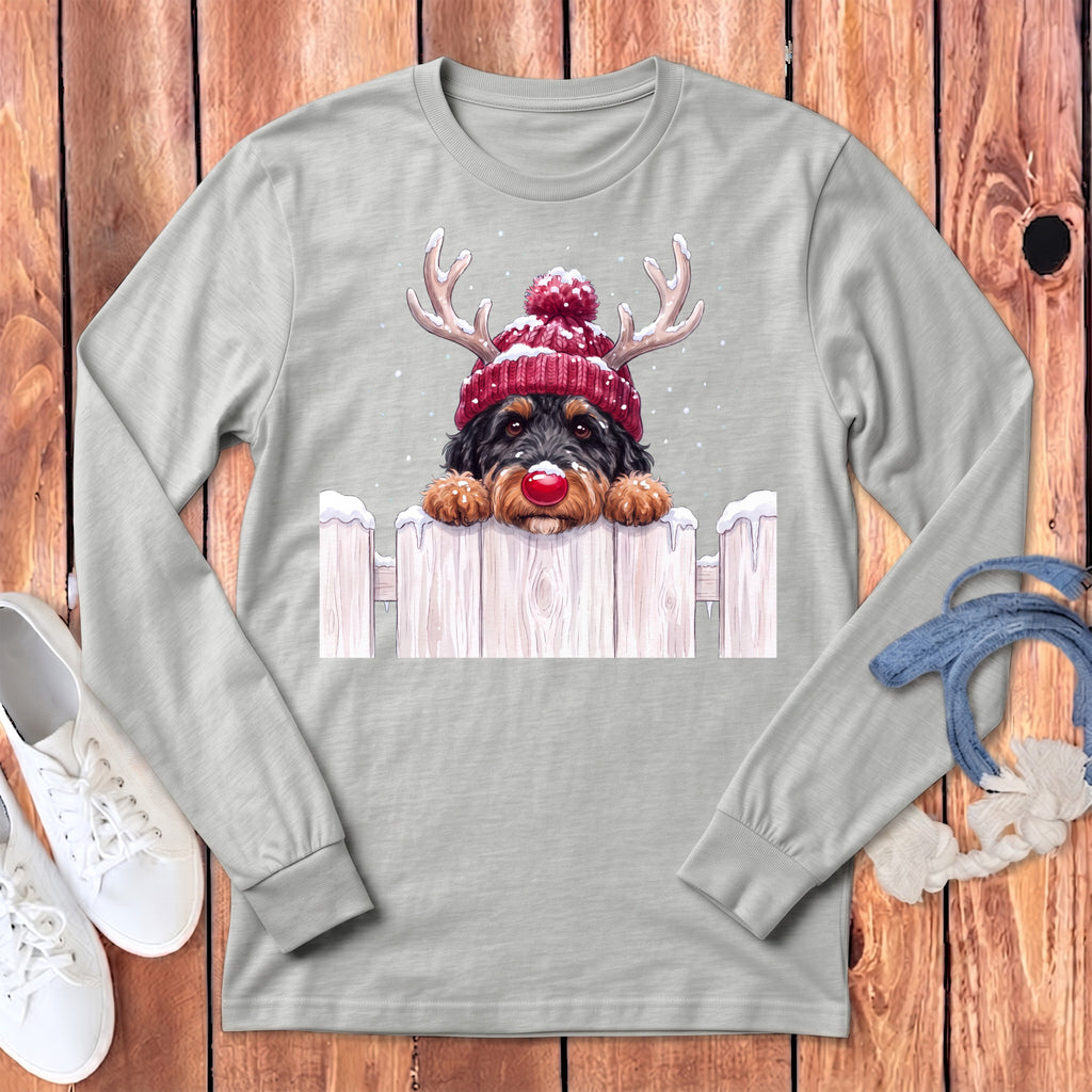 Dog wearing a red reindeer hat and red nose, peeking over a snowy fence.
