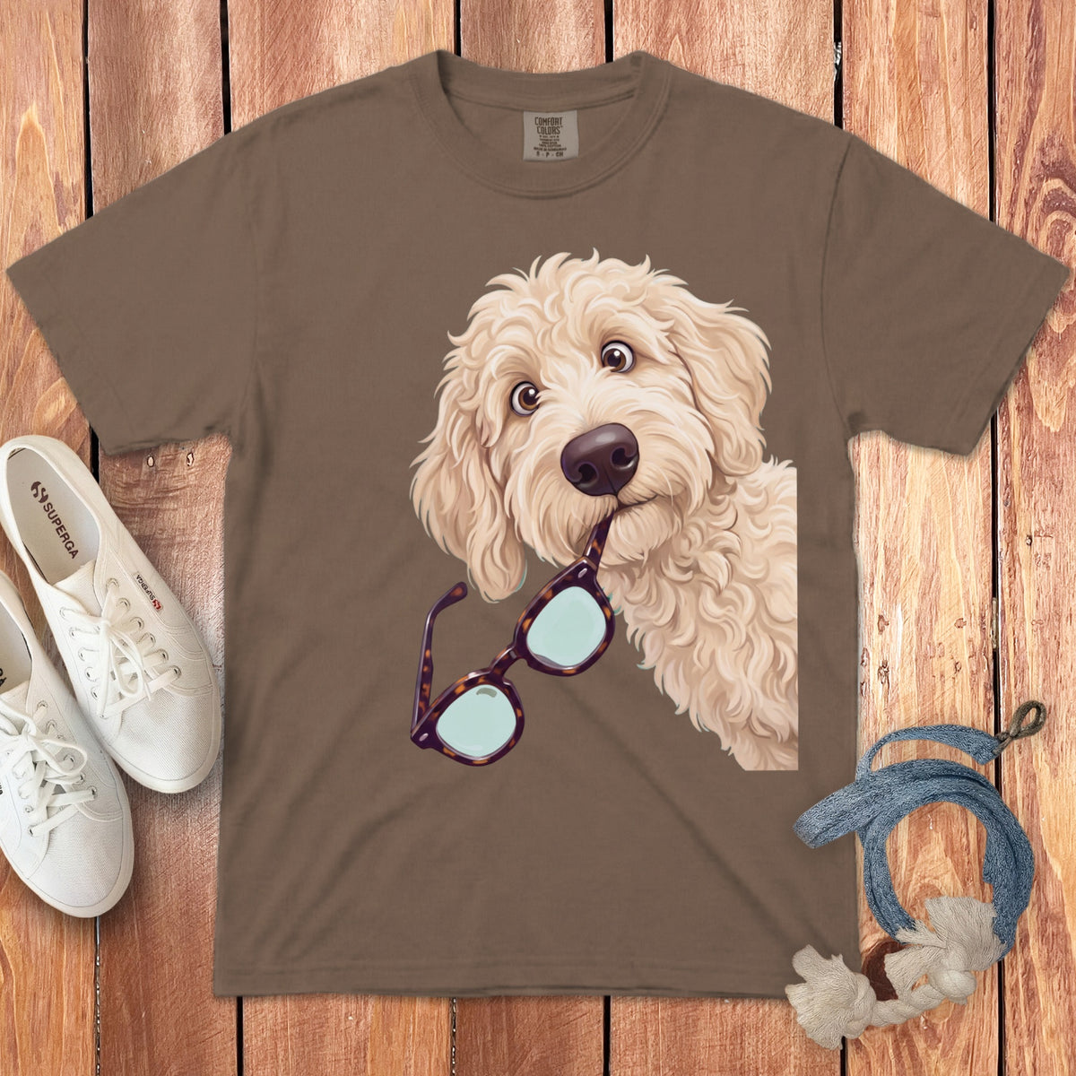 Brown t-shirt featuring an illustrated golden doodle dog holding tortoiseshell glasses in its mouth.