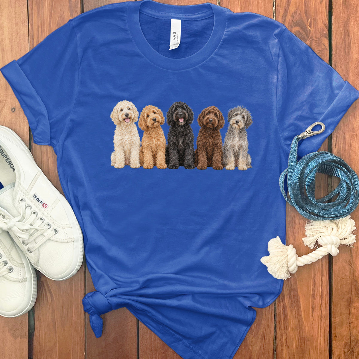 Five fluffy dogs in different colors sit in a line on a blue t-shirt.