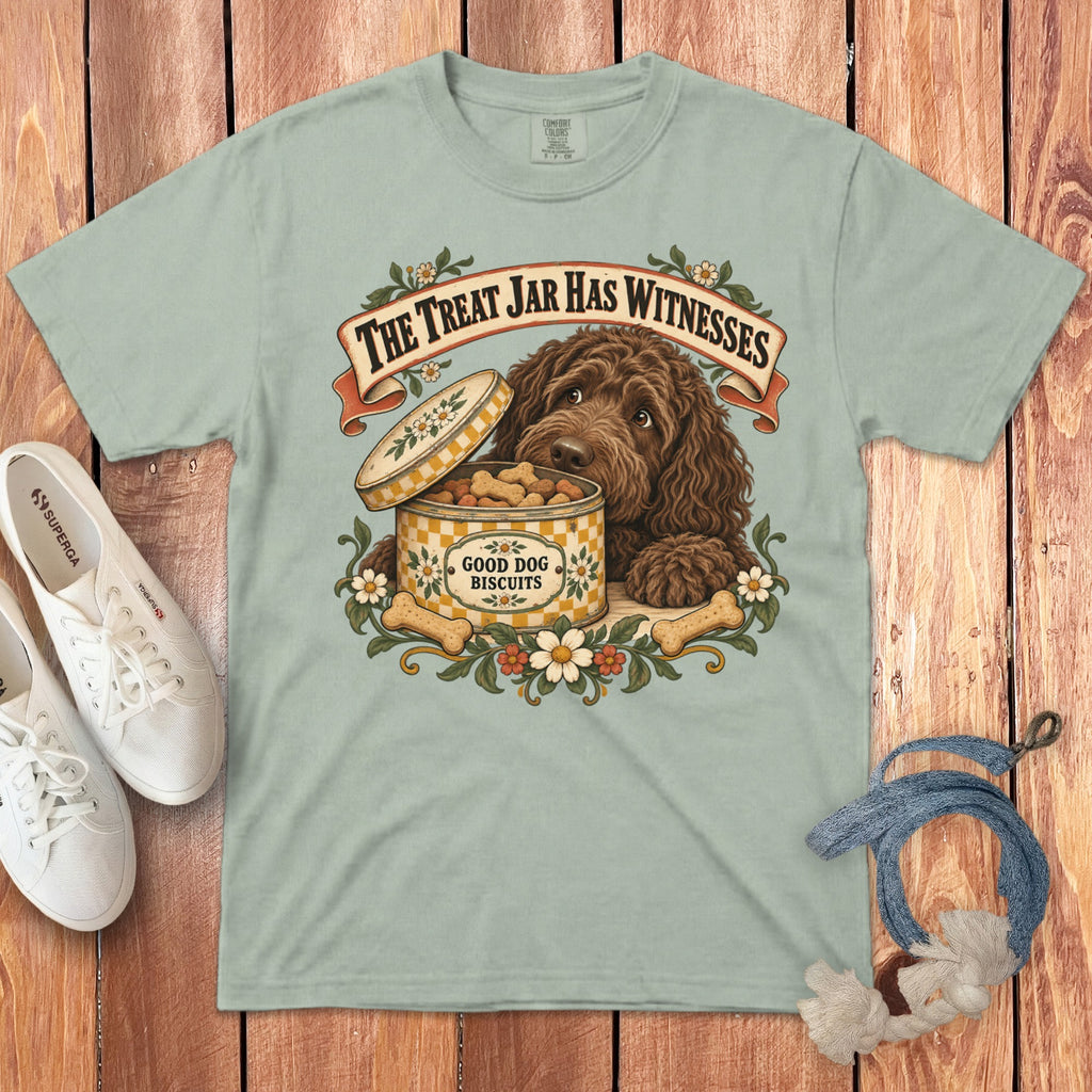 Sage green t-shirt with a vintage graphic of a brown dog and biscuit tin on wooden background.