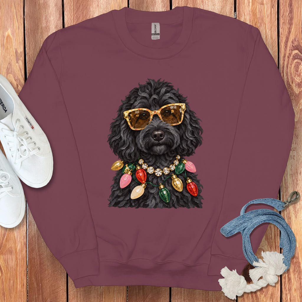 Black poodle wearing sunglasses and colorful Christmas lights necklace on maroon sweatshirt.