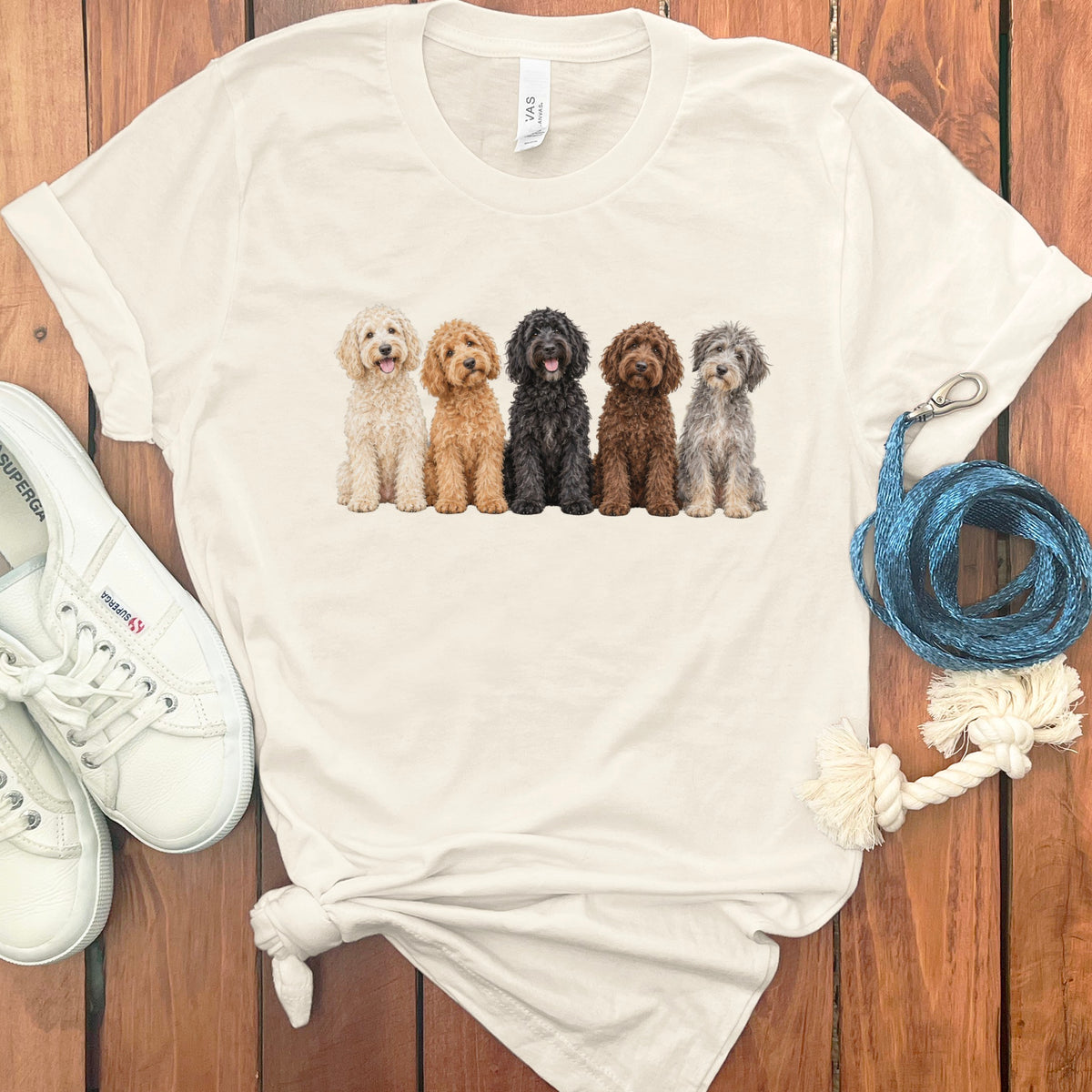 Cream t-shirt with a print of five different colored doodle dogs sitting in a row.