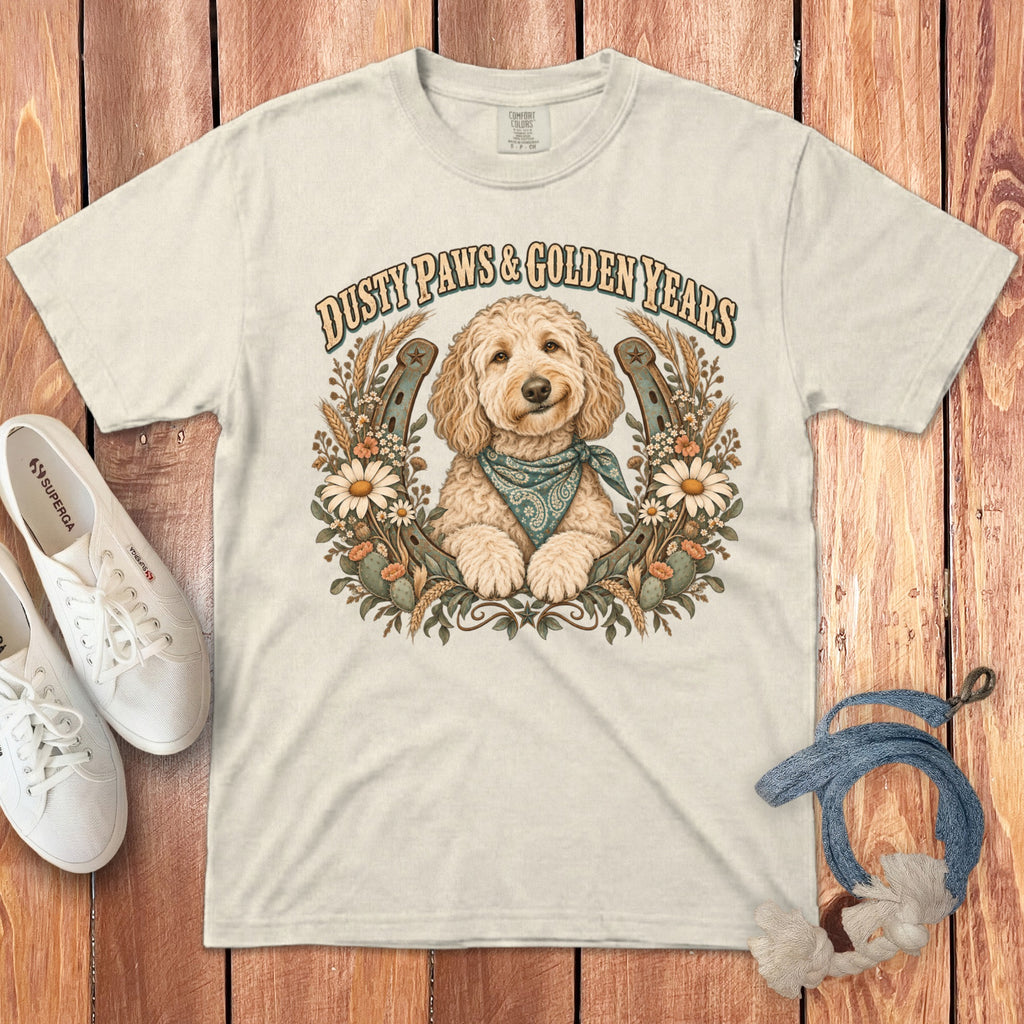 A cream-colored t-shirt with a golden doodle graphic, horseshoe, flowers, and Dusty Paws and Golden Years text.