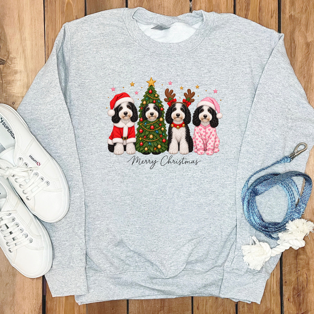 A light gray crewneck sweatshirt featuring a graphic of four dogs, a Christmas tree, and the text "Merry Christmas".