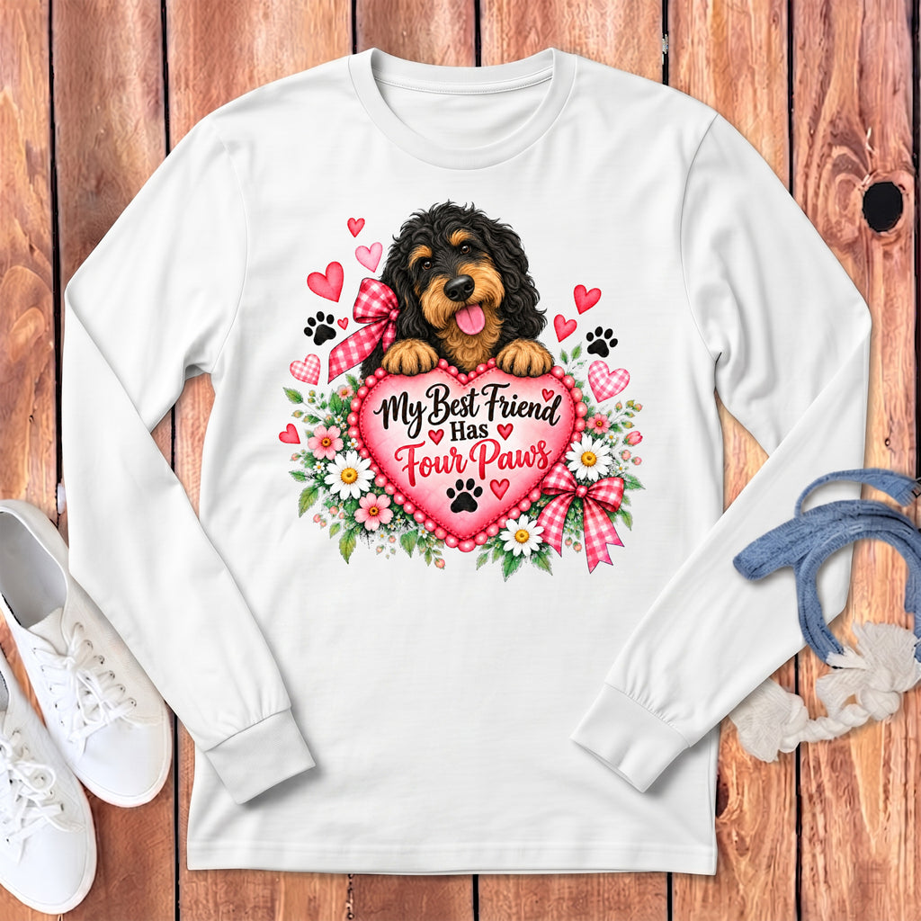 A white long-sleeved shirt features a graphic of a black and tan dog behind a pink heart with the text My Best Friend Has Four Paws, surrounded by flowers and paw prints.