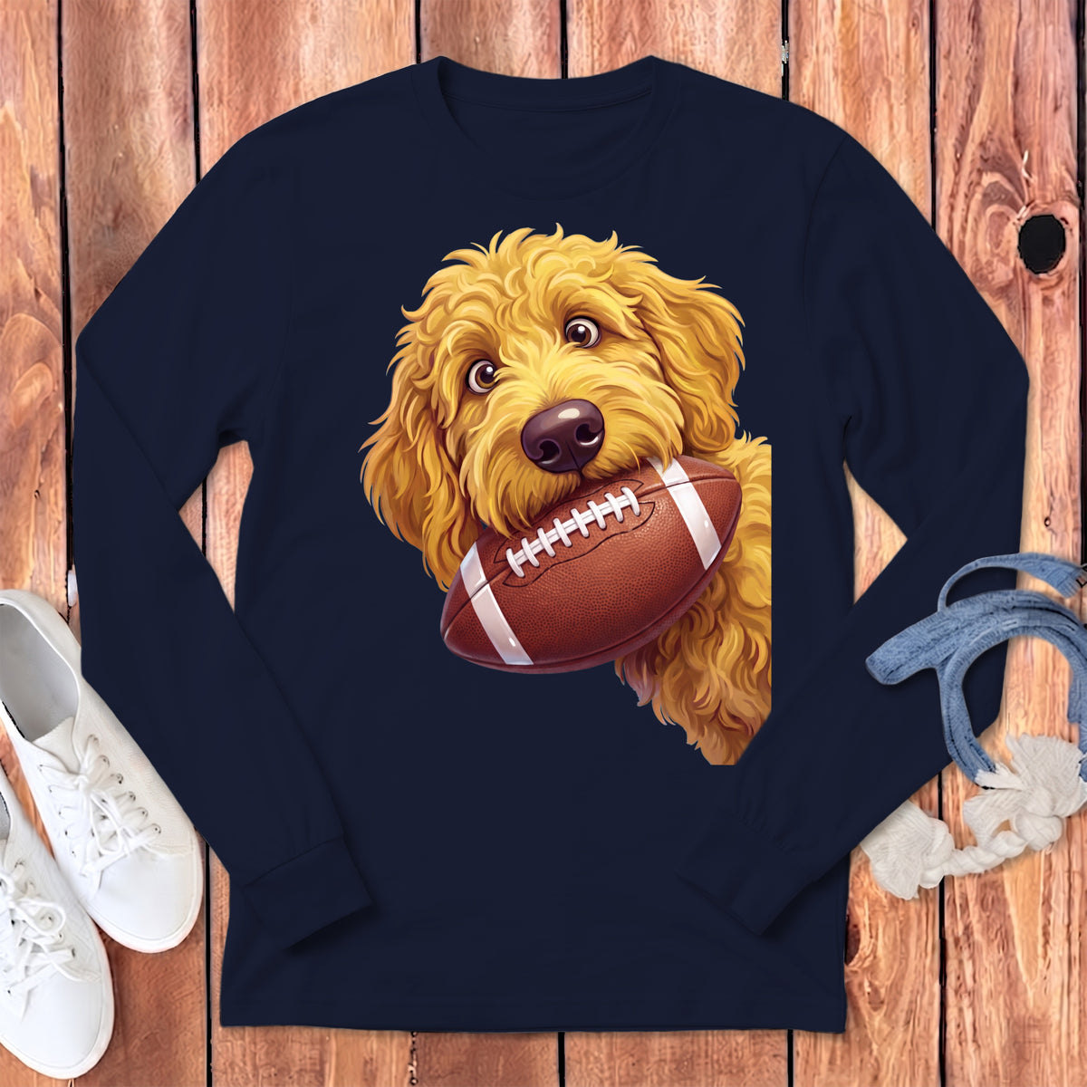 Goldendoodle puppy with a football in its mouth on a navy long-sleeve shirt.