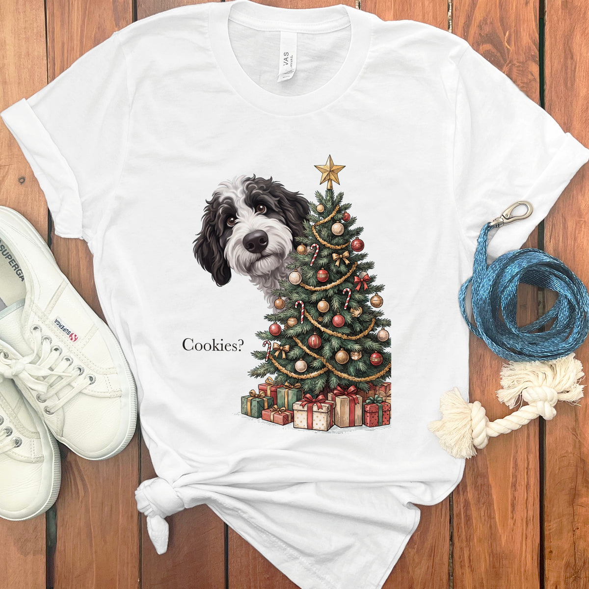 Black and white dog peeking from behind a Christmas tree with gifts and text "Cookies?".