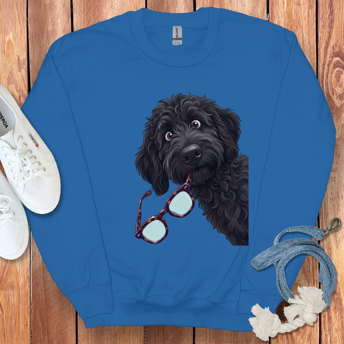 A bright blue crewneck sweatshirt featuring an illustration of a black doodle dog holding glasses in its mouth.