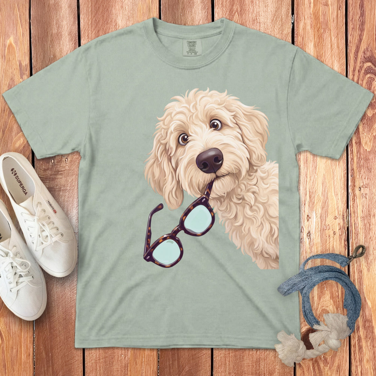 Light green t-shirt with a cartoon illustration of a fluffy golden doodle holding glasses.