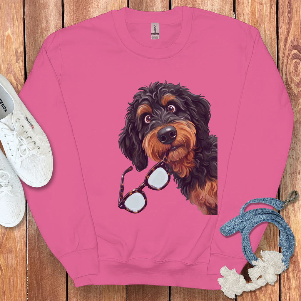 Pink crewneck sweatshirt featuring a graphic of a black and tan doodle dog holding glasses.