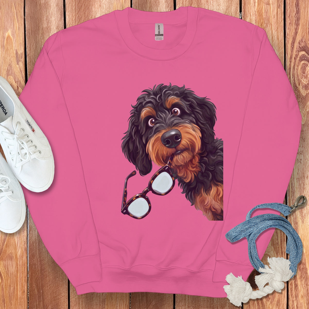 Pink crewneck sweatshirt featuring a graphic of a black and tan doodle dog holding glasses.