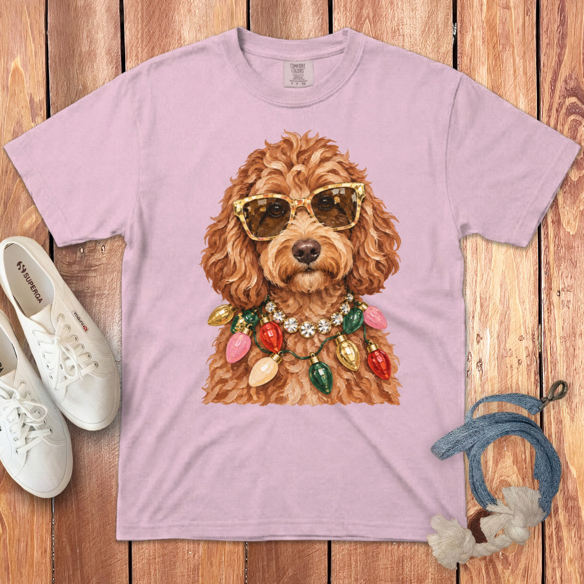 Pink t-shirt with a watercolor illustration of a goldendoodle wearing sunglasses and a string of colorful Christmas lights.