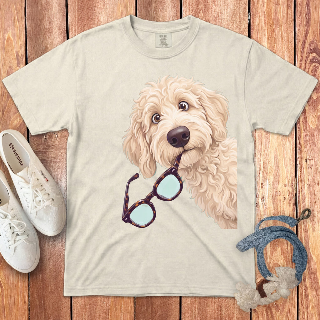 Beige t-shirt featuring a cartoon golden doodle dog holding tortoiseshell glasses in its mouth.
