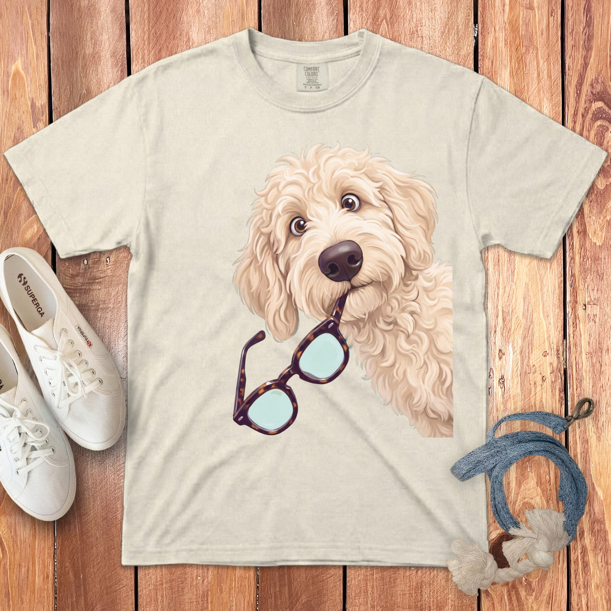 Beige t-shirt featuring a cartoon golden doodle dog holding tortoiseshell glasses in its mouth.